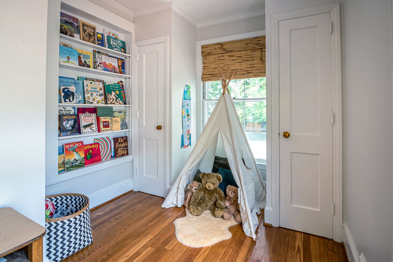 Home Charming children's room featuring a play tent, stuffed toys, and a bookshelf filled with colorful books.